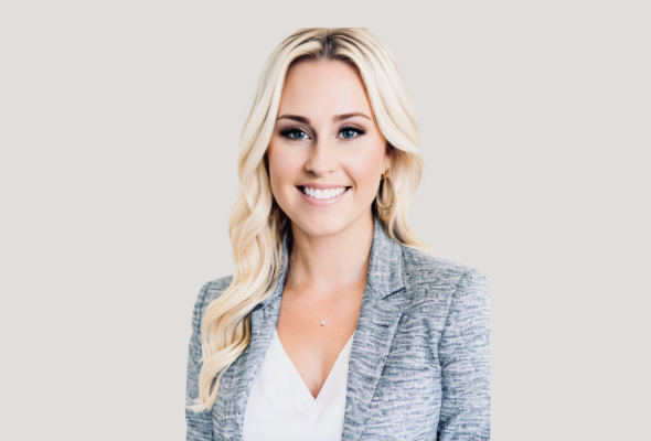 Professional woman smiling in grey blazer against light background.