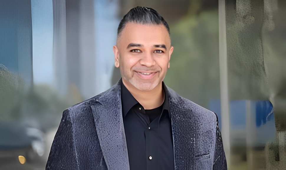 Man in dark jacket smiling confidently in professional portrait setting.